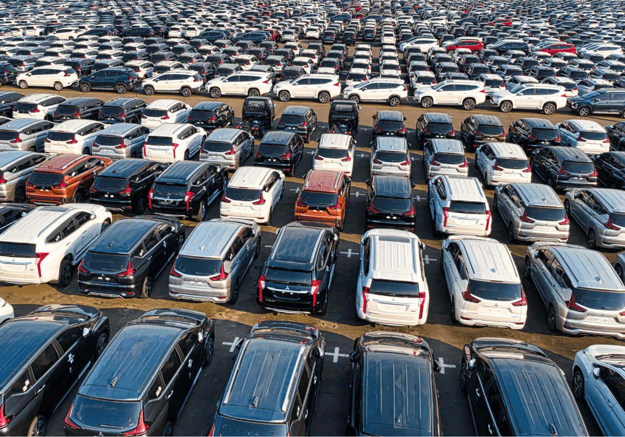 Aerial view of a vast parking lot filled with hundreds of new cars, neatly arranged in rows.