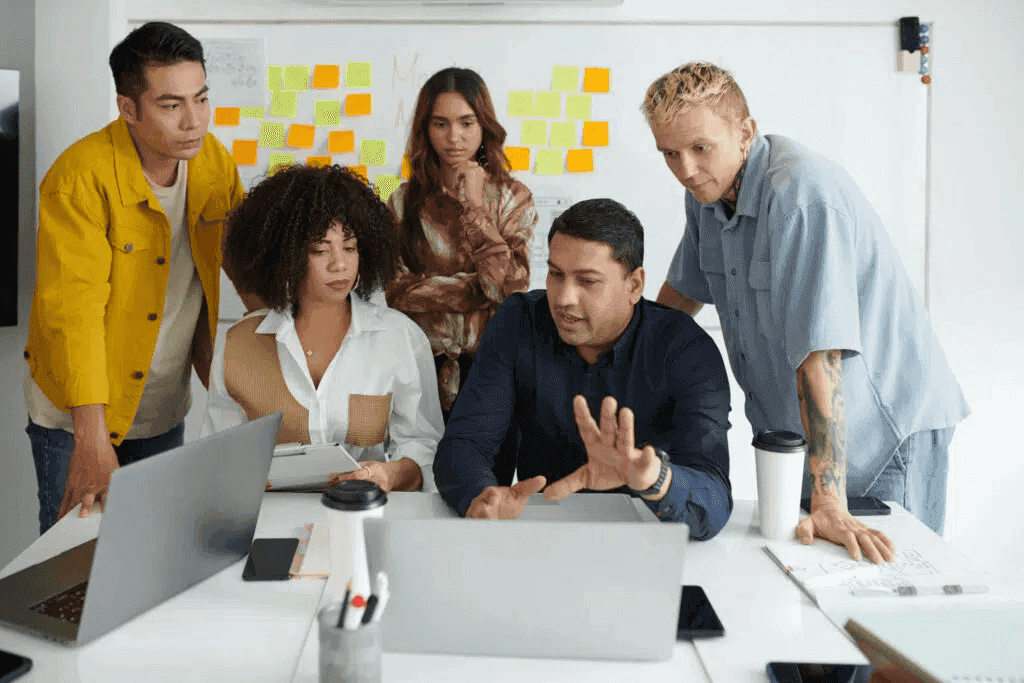 A candid picture of five colleagues working together in a conference room looking at something on someone's laptop.