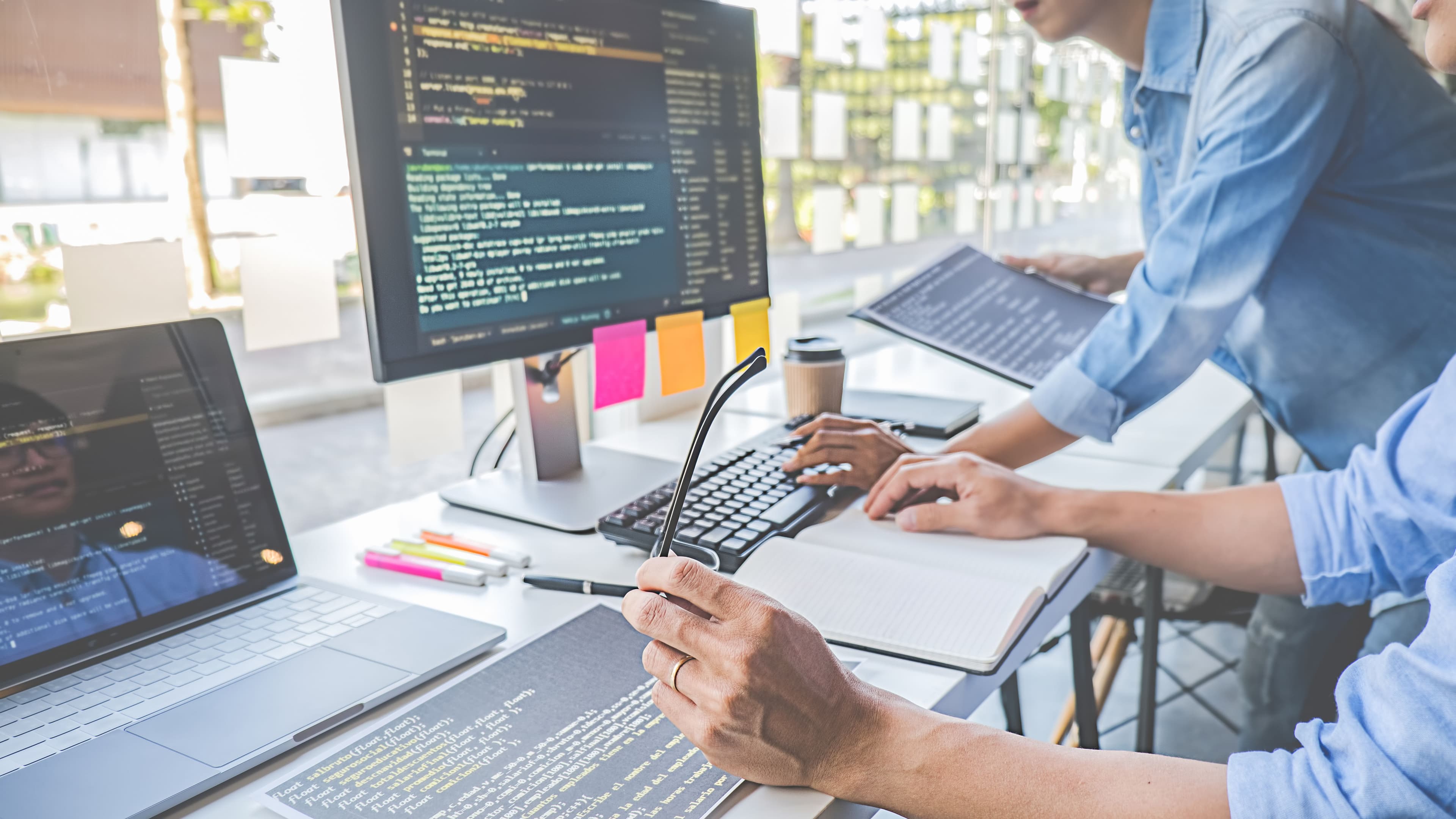 Two men sitting at a large desk looking at code on a computer.