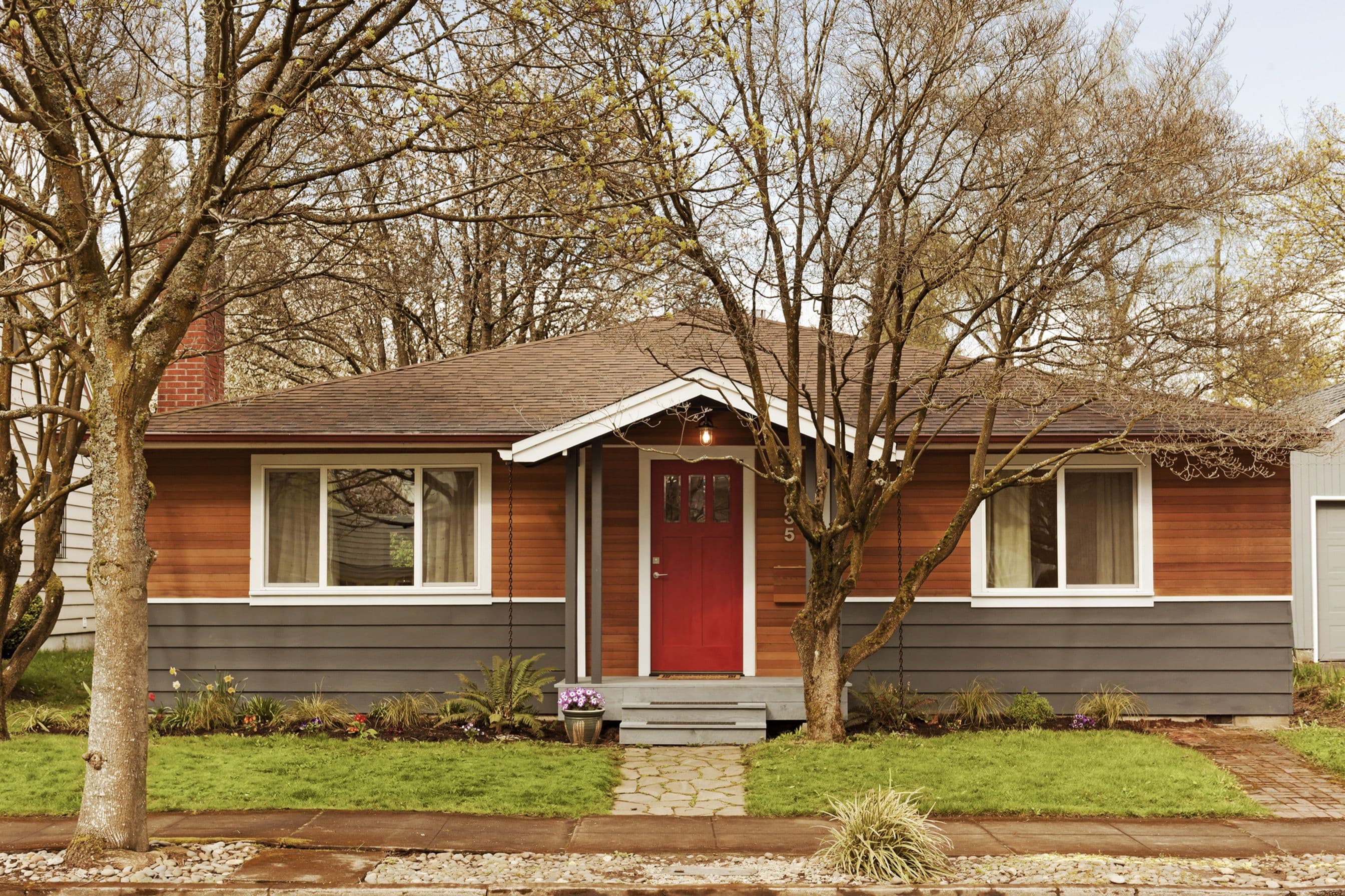 A single-level ranch house with some trees and the front yard.